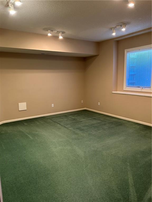 basement with dark colored carpet, baseboards, a textured ceiling, and track lighting