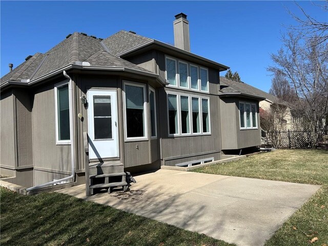 rear view of property featuring a lawn, entry steps, fence, a shingled roof, and a chimney