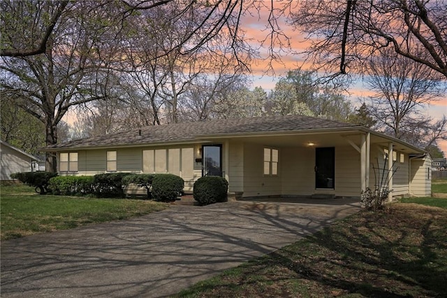 ranch-style house with asphalt driveway, an attached carport, and a lawn