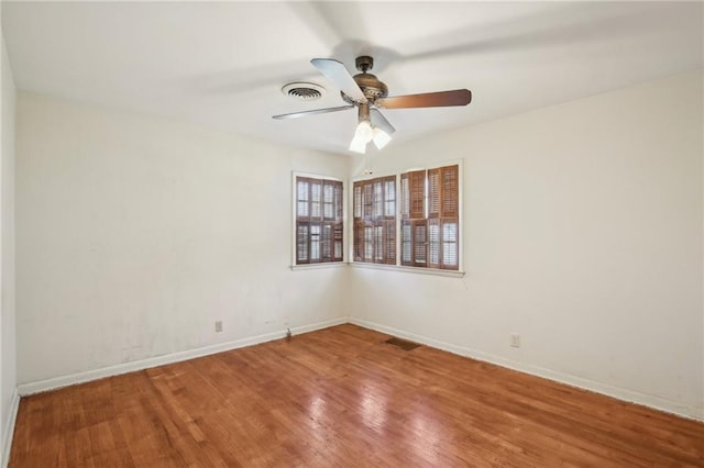 spare room with wood finished floors, a ceiling fan, and baseboards