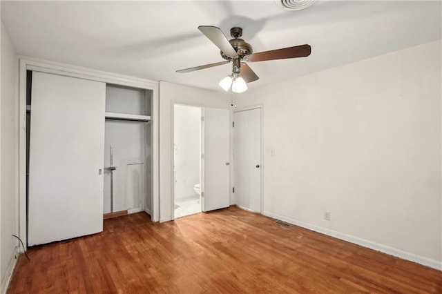 unfurnished bedroom featuring wood finished floors, a closet, ensuite bath, ceiling fan, and baseboards