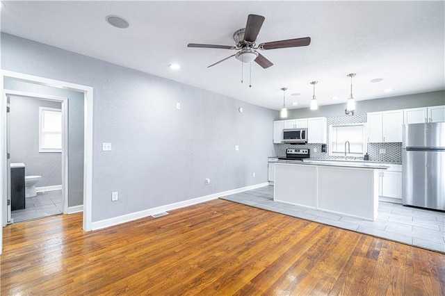 kitchen featuring pendant lighting, appliances with stainless steel finishes, white cabinetry, light hardwood / wood-style floors, and decorative backsplash