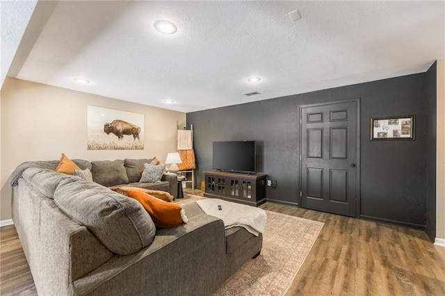 living room featuring a textured ceiling, baseboards, wood finished floors, and recessed lighting