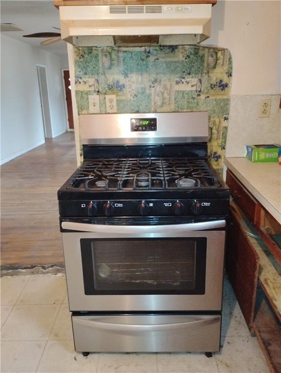 kitchen with tasteful backsplash, light tile patterned floors, stainless steel gas range oven, and ceiling fan