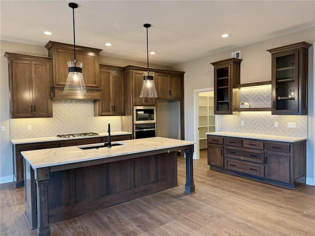 kitchen featuring hanging light fixtures, a kitchen breakfast bar, an island with sink, stainless steel gas stovetop, and light stone countertops