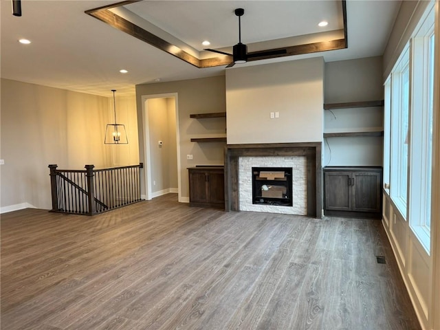 unfurnished living room with wood-type flooring, a stone fireplace, and a raised ceiling