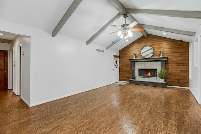 unfurnished living room with wooden walls, a fireplace, lofted ceiling with beams, wood-type flooring, and ceiling fan