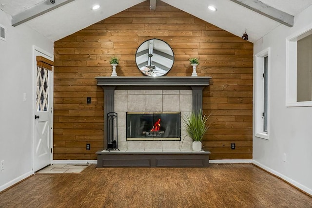 interior details featuring a tiled fireplace, hardwood / wood-style flooring, wooden walls, and beam ceiling