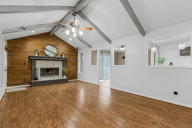 unfurnished living room featuring lofted ceiling with beams, wooden walls, hardwood / wood-style flooring, ceiling fan, and a tiled fireplace