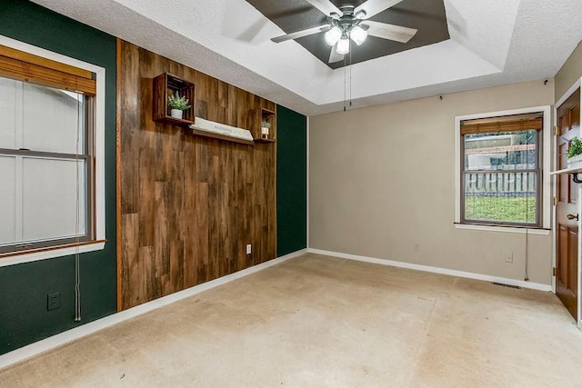 spare room with a tray ceiling, a textured ceiling, ceiling fan, and wood walls