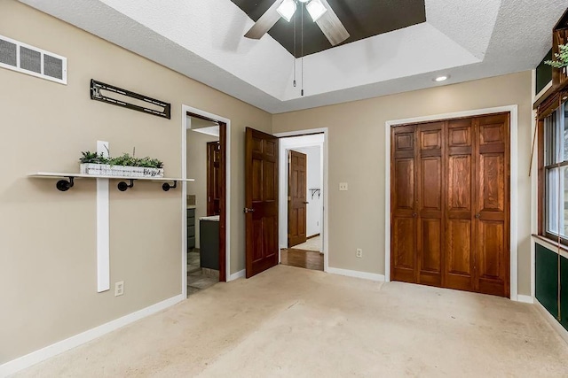 unfurnished bedroom featuring connected bathroom, ceiling fan, a raised ceiling, light carpet, and a closet