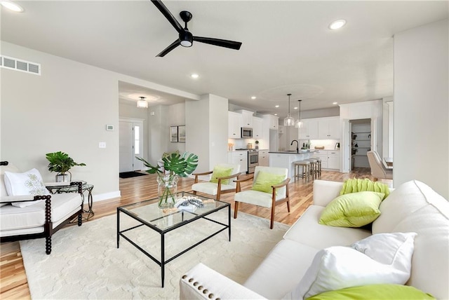 living room with sink, ceiling fan, and light hardwood / wood-style flooring