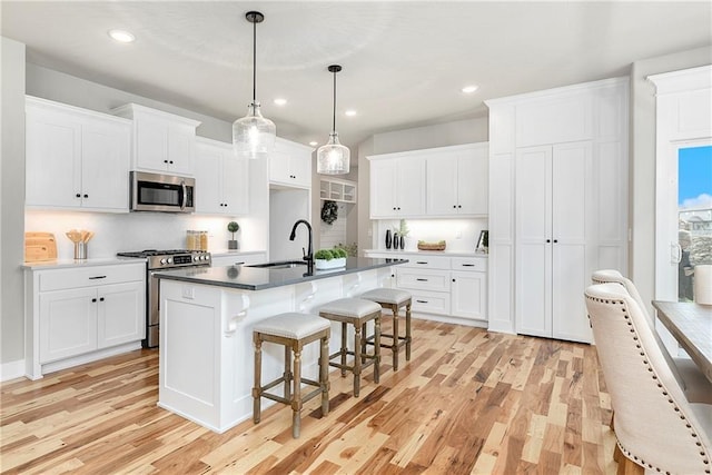 kitchen with sink, white cabinetry, stainless steel appliances, a center island with sink, and decorative light fixtures