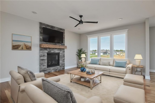 living room featuring ceiling fan, a stone fireplace, and hardwood / wood-style floors