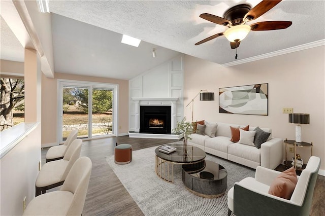 living room with lofted ceiling, a ceiling fan, a large fireplace, a textured ceiling, and wood finished floors