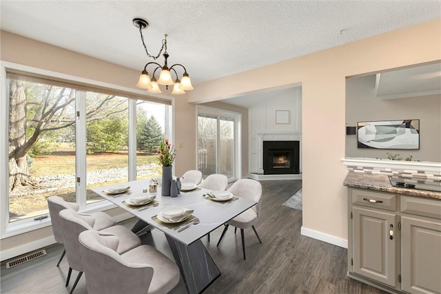 dining area featuring a chandelier, a warm lit fireplace, a textured ceiling, visible vents, and dark wood-style floors