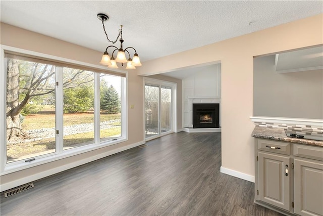 unfurnished dining area with a warm lit fireplace, a textured ceiling, visible vents, dark wood finished floors, and an inviting chandelier