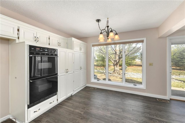 kitchen featuring dobule oven black, white cabinets, dark wood-type flooring, and an inviting chandelier