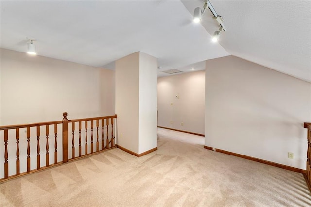 carpeted empty room featuring vaulted ceiling, track lighting, and baseboards