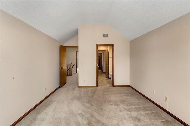 unfurnished bedroom featuring vaulted ceiling, baseboards, visible vents, and light colored carpet