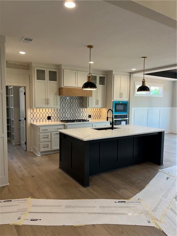 2209 W 176th Pl, Overland Park, KS 66085 - kitchen with built in microwave, light wood finished floors, gas stovetop, backsplash, and a center island with sink