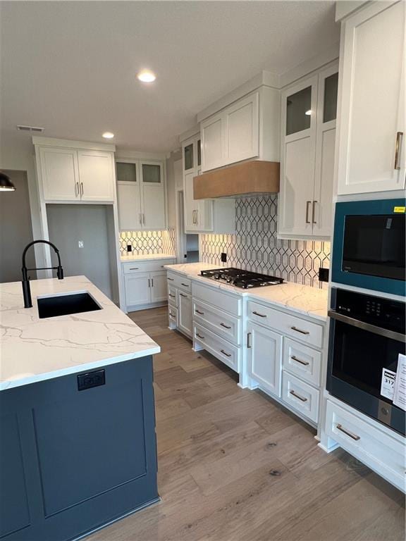 2209 W 176th Pl, Overland Park, KS 66085 - kitchen with appliances with stainless steel finishes, light stone countertops, wood finished floors, white cabinetry, and decorative backsplash