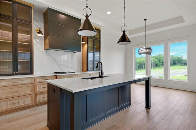 24909 W 98th Pl, Lenexa, KS 66227 - kitchen featuring light wood finished floors, backsplash, a center island with sink, a raised ceiling, and glass insert cabinets