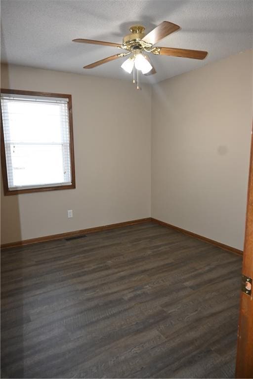 empty room with ceiling fan, dark wood-type flooring, and a textured ceiling