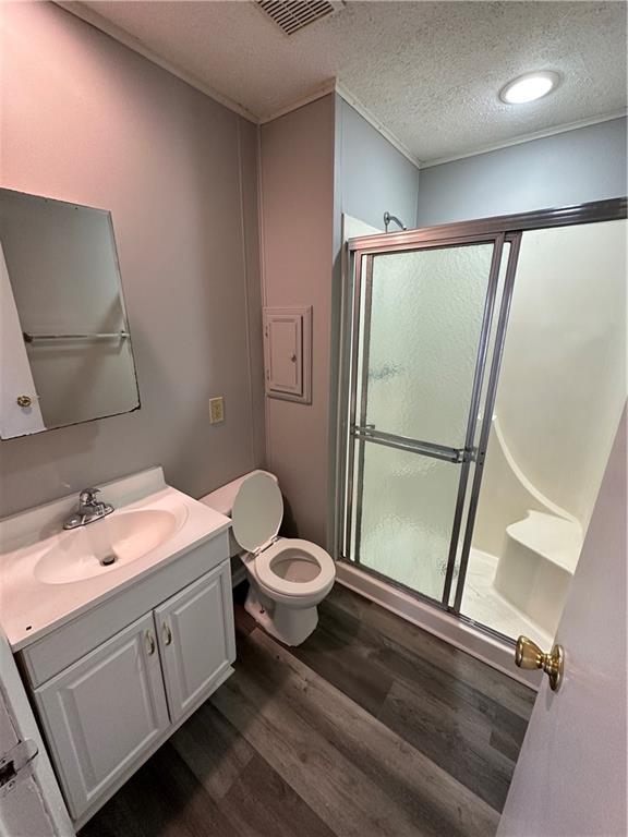 bathroom featuring a shower with door, hardwood / wood-style floors, vanity, a textured ceiling, and toilet