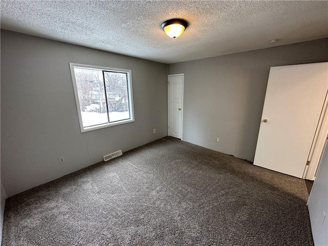 spare room featuring dark carpet and a textured ceiling