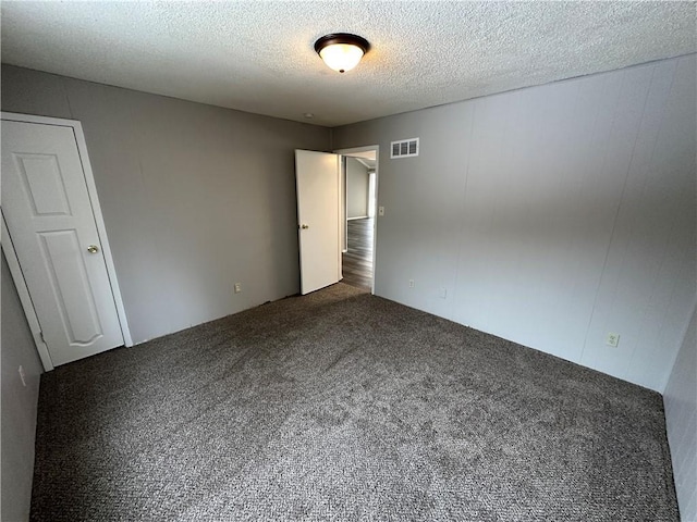 unfurnished bedroom with a textured ceiling and dark colored carpet