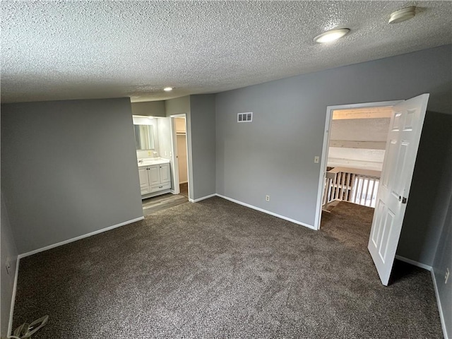 unfurnished bedroom featuring connected bathroom, a textured ceiling, and dark carpet