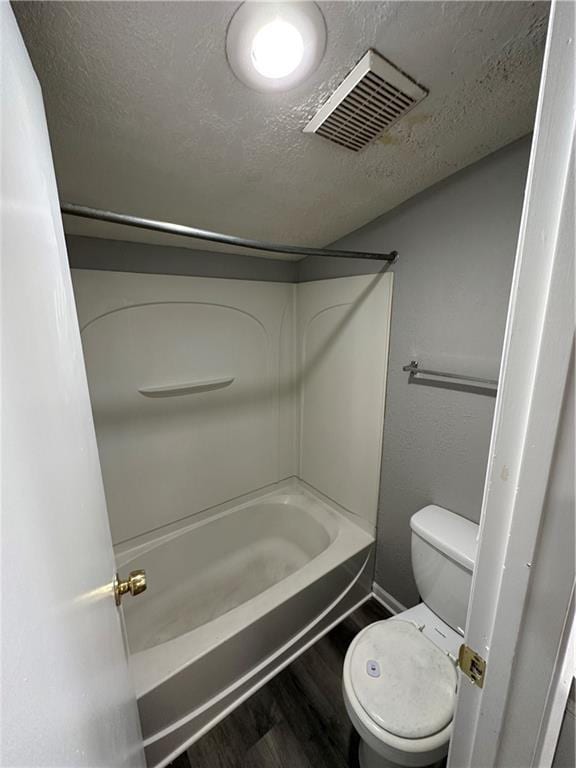 bathroom featuring wood-type flooring, shower / tub combination, toilet, and a textured ceiling