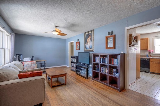 living area with a textured ceiling, visible vents, baseboards, a ceiling fan, and light wood finished floors