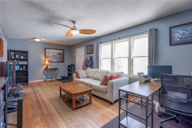 living room with ceiling fan, a textured ceiling, baseboards, and wood finished floors