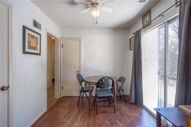 dining space with dark wood-style floors, visible vents, a textured ceiling, and a ceiling fan