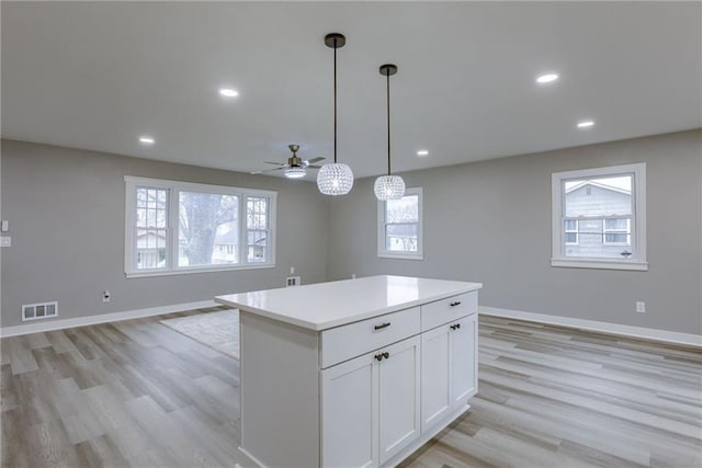 kitchen featuring pendant lighting, light hardwood / wood-style flooring, ceiling fan, a center island, and white cabinets