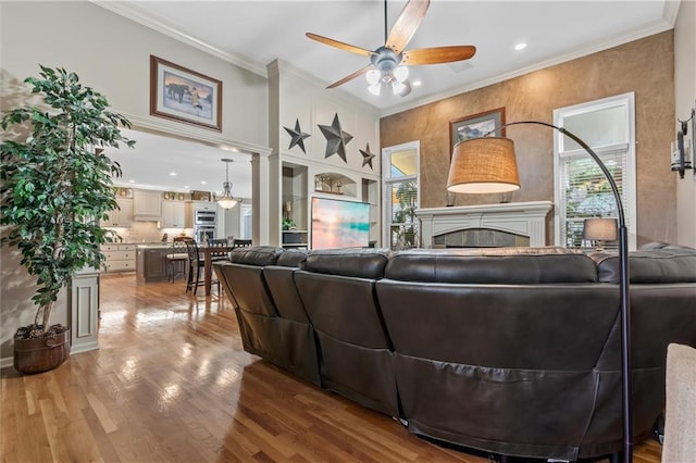 living area with a ceiling fan, crown molding, and wood finished floors