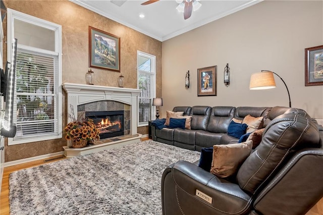 living room featuring ceiling fan, wood finished floors, baseboards, ornamental molding, and a tiled fireplace