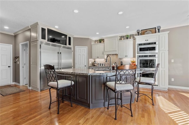 kitchen featuring an island with sink, a breakfast bar area, ornamental molding, light stone countertops, and a sink