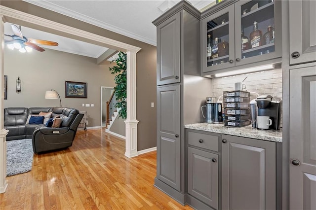 bar with decorative backsplash, ornamental molding, a ceiling fan, light wood-style floors, and stairs