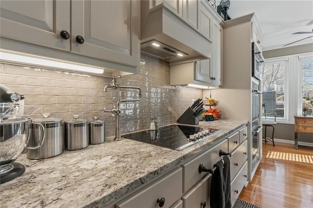 kitchen with light wood-style floors, gray cabinets, custom range hood, and black electric cooktop