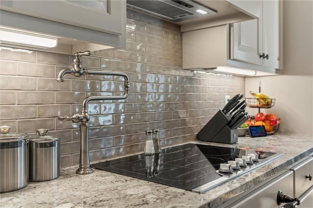 kitchen with light stone countertops, black electric cooktop, backsplash, and exhaust hood