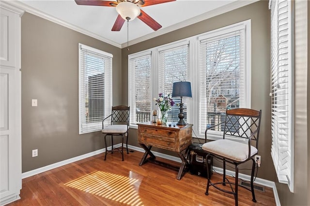 living area with baseboards, visible vents, a ceiling fan, ornamental molding, and wood finished floors