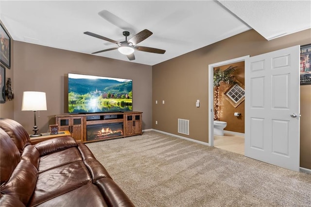 living area with light colored carpet, visible vents, a glass covered fireplace, ceiling fan, and baseboards