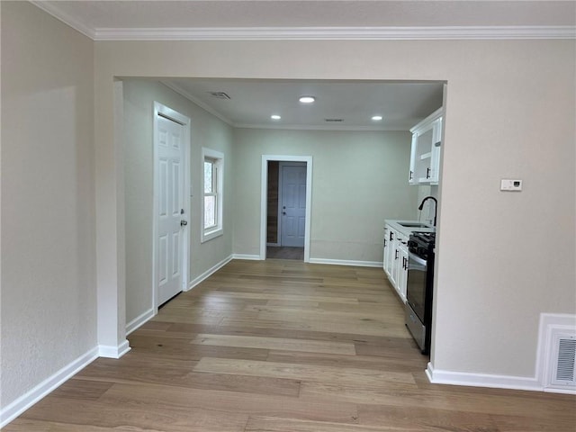 kitchen featuring sink, white cabinets, ornamental molding, gas stove, and light wood-type flooring