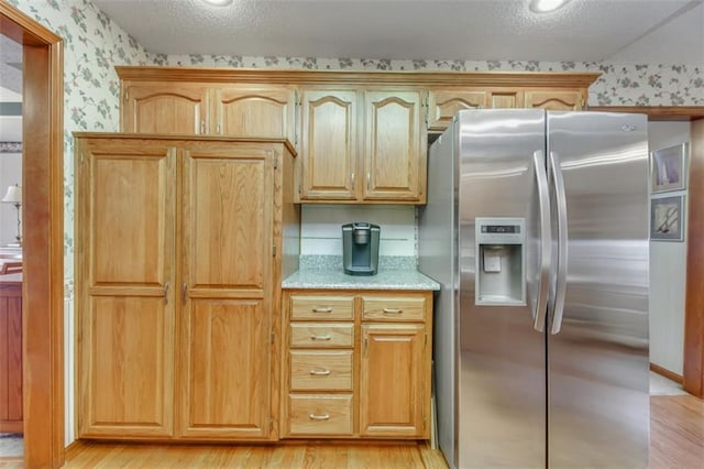 kitchen featuring stainless steel fridge, light hardwood / wood-style floors, a textured ceiling, and light brown cabinets