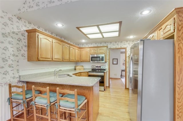 kitchen with sink, light hardwood / wood-style flooring, appliances with stainless steel finishes, a kitchen bar, and kitchen peninsula