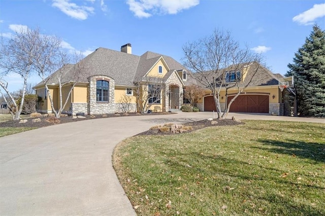 french country home featuring driveway, a front lawn, stone siding, an attached garage, and a chimney