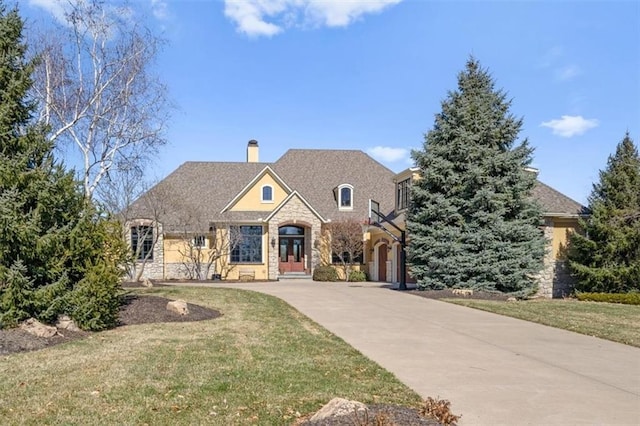 view of front facade featuring a front lawn, stone siding, french doors, concrete driveway, and a chimney